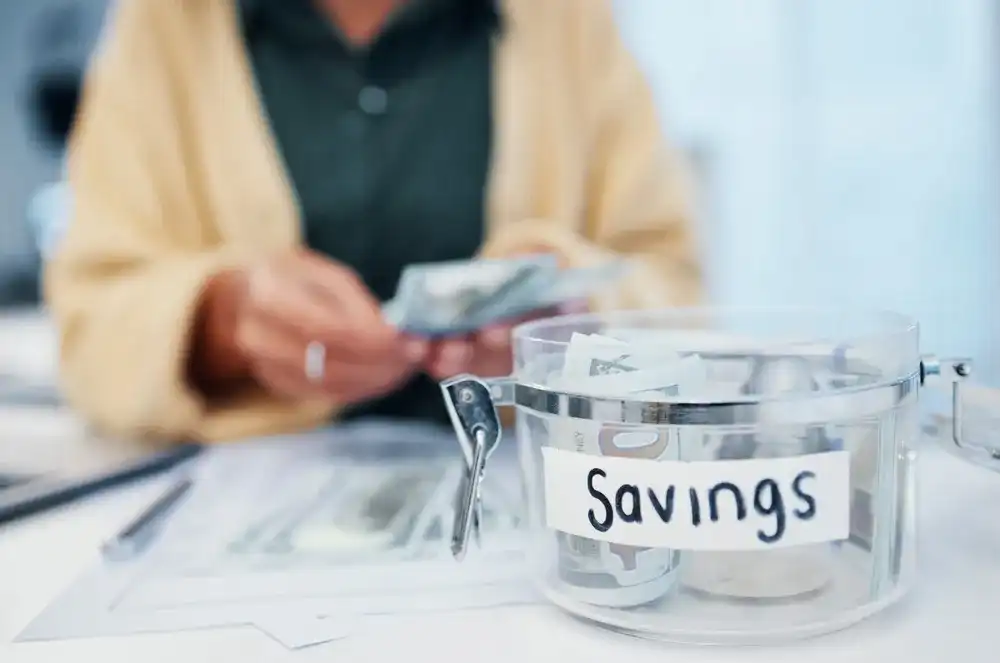 Someone putting money in a container that reads "Savings"