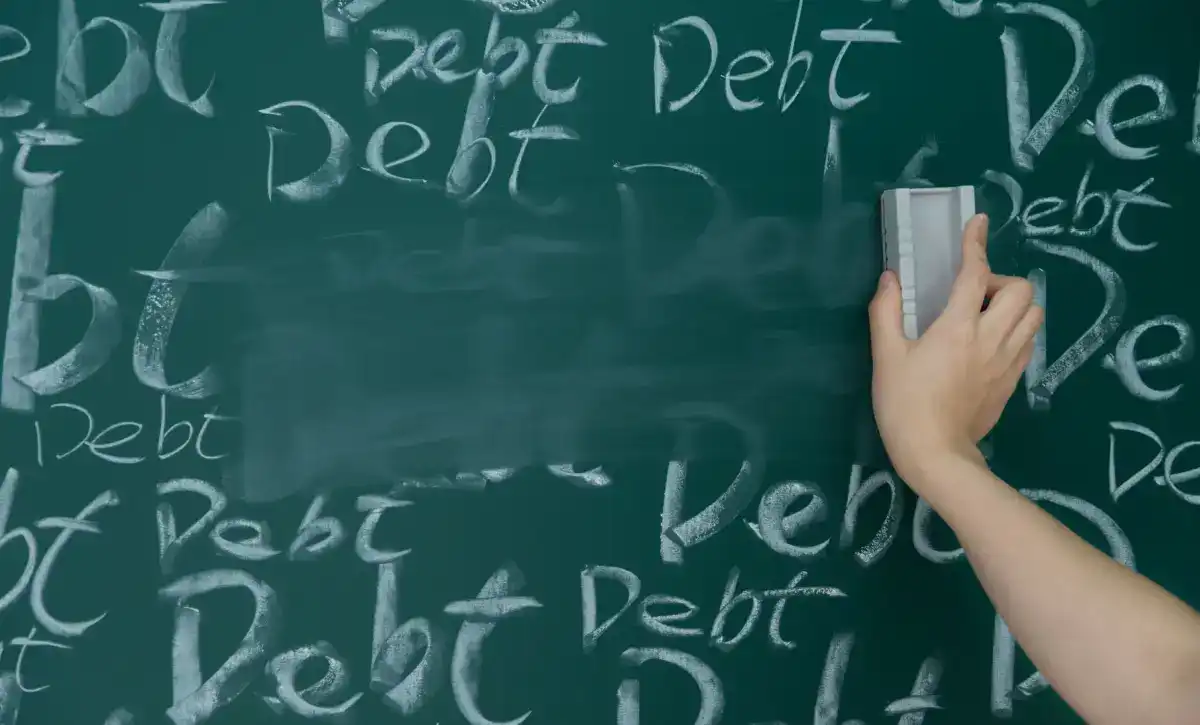 Person wiping away the word debt from a chalkboard