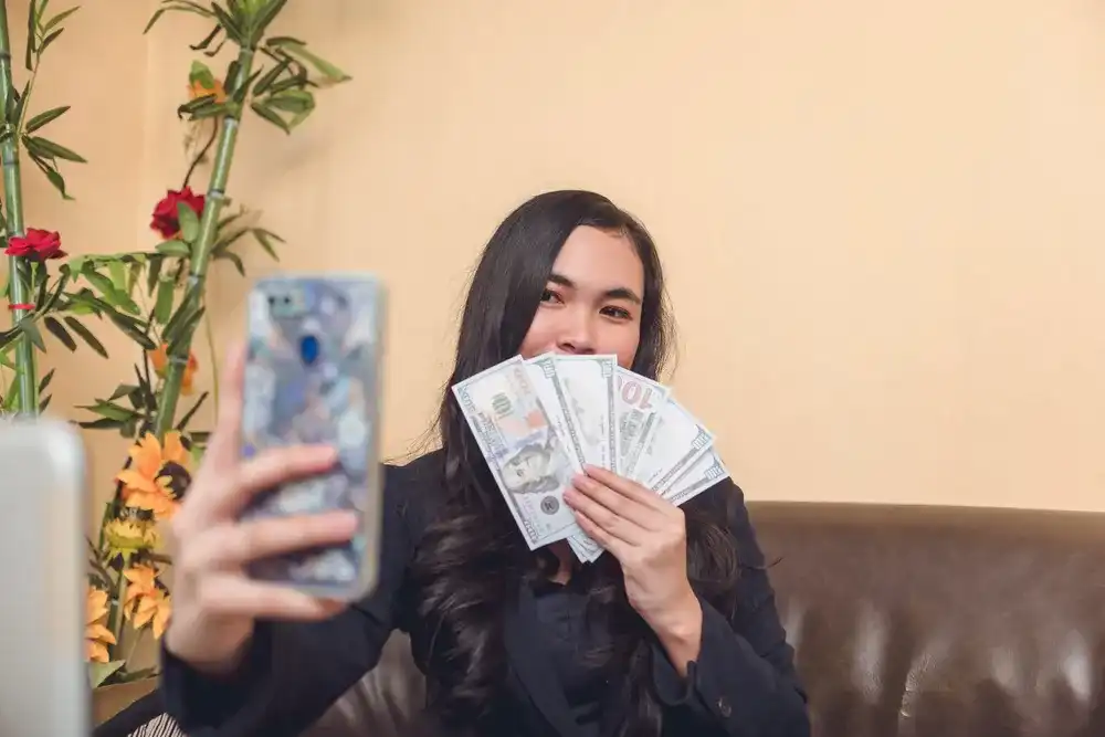 A Gen Z woman taking a selfie with $100 bills