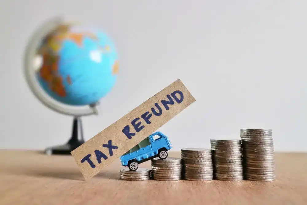 A toy car towing a sign reading "Tax Refund" atop a stack of coins