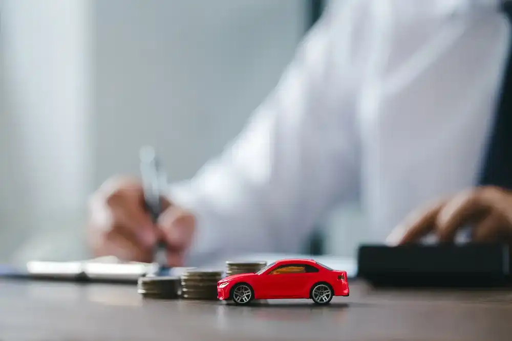 A toy car next to a stack of coins in front of someone signing an auto equity loan
