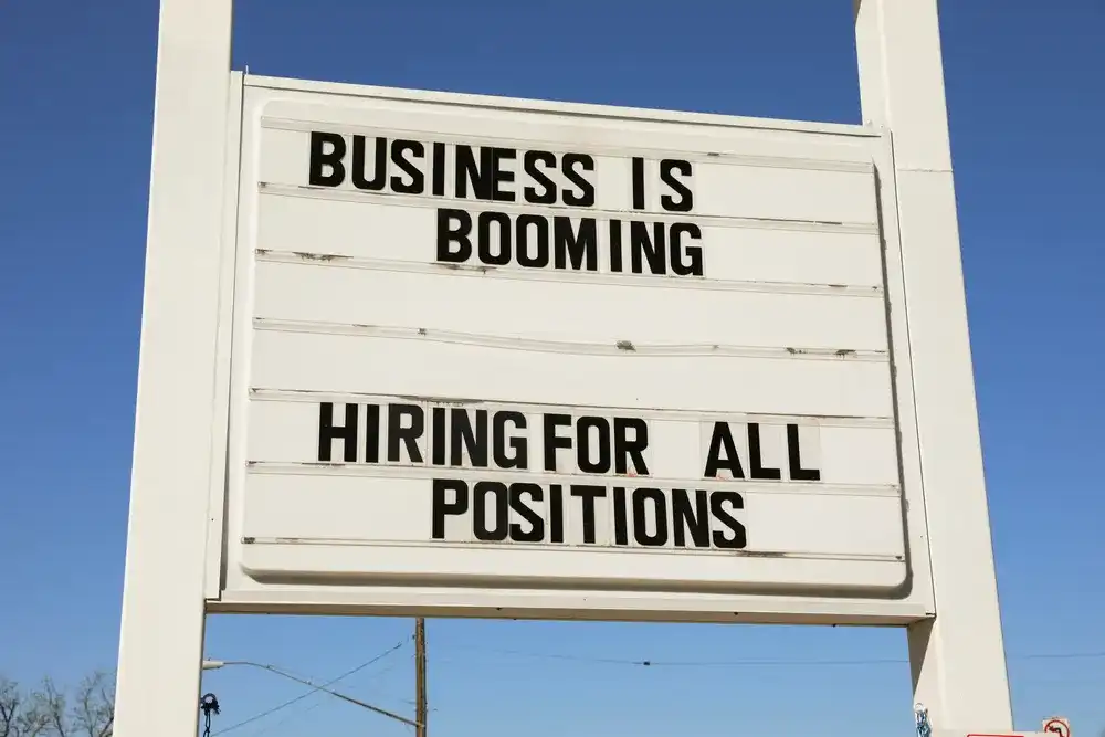 Store sign reading "Business is booming, Hiring for all Positions"