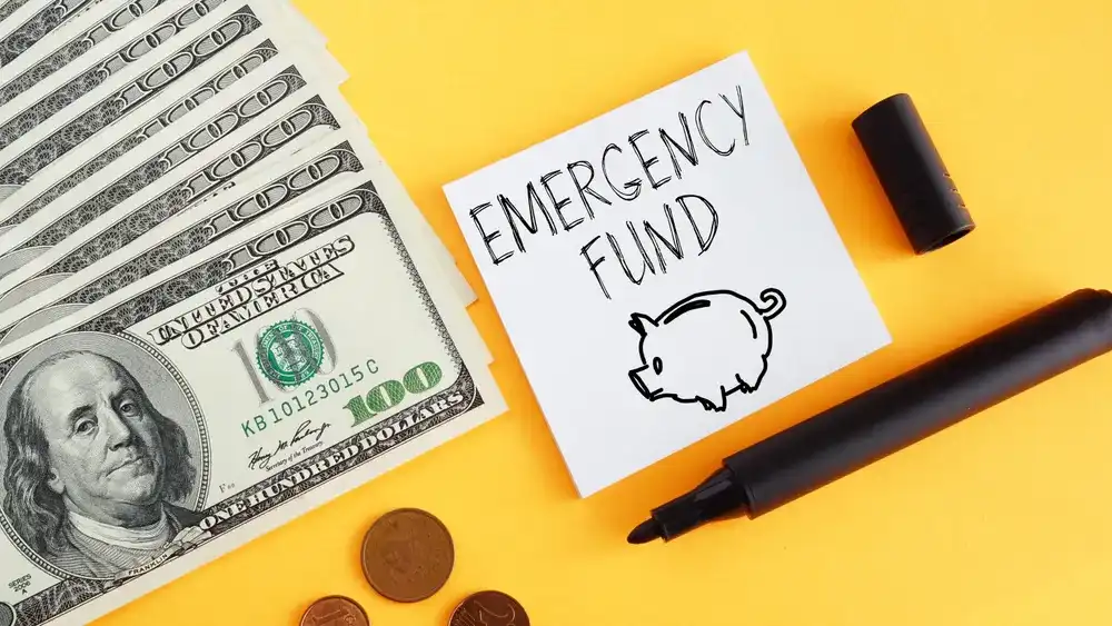$100 bills next to a sticky note that reads "Emergency Fund"