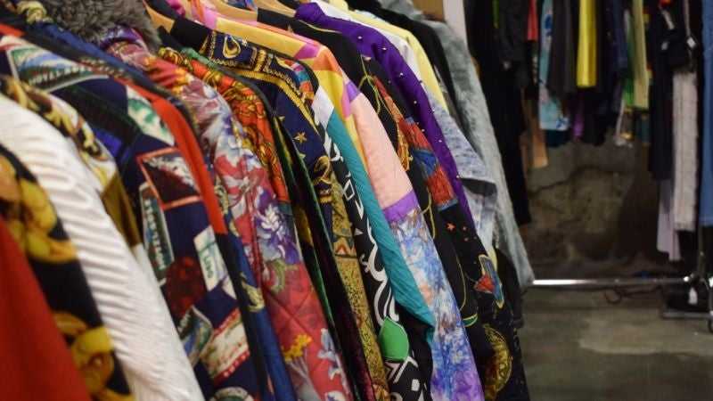 Vibrant shirts and vintage jackets on a thrift store rack.